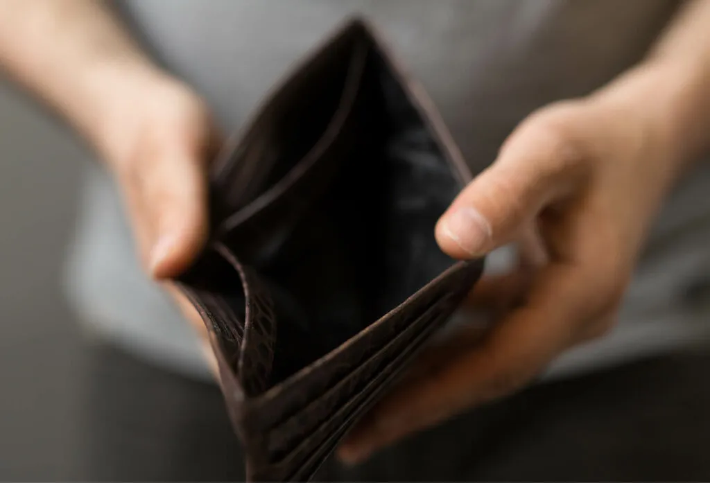 En man i fattigdom håller upp en tom plånbok mot kameran.