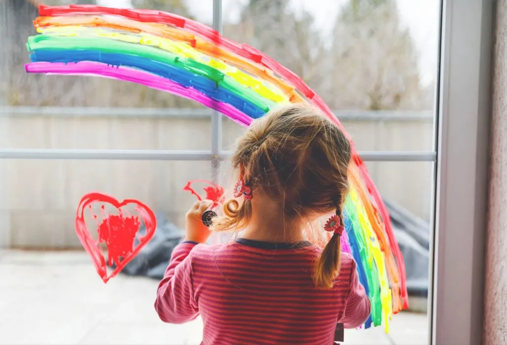 Ett litet barn, en flicka, står och målar en regnbåge och ett hjärta i en mötesplats för bostadslösa barnfamiljer i Stockholm som kallas för Trygga rum.