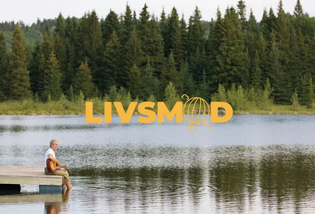 En äldre man sitter på en brygga och spelar gitarr med fötterna i vattnet omgärdat av grönska. Över bilden är loggan LIVSMOD.