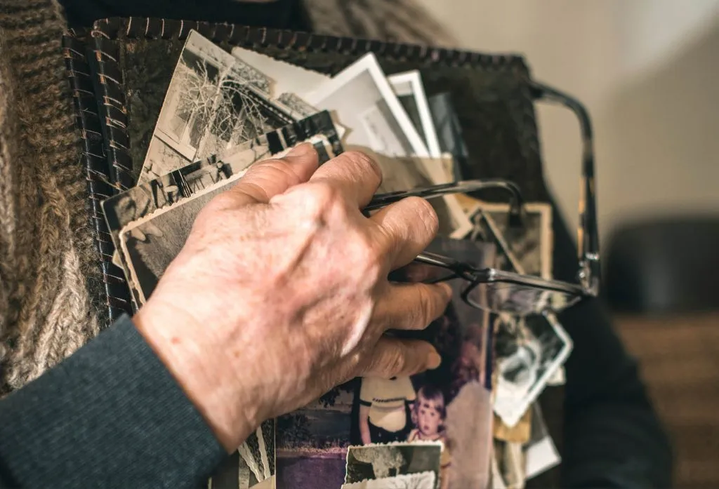 Bild på en äldre människas händer som håller i en mängd fotografier. Symbol för de minnen vi bär på efter ett långt liv, och en beskrivande bild för de samtalsgrupper för äldre som Sociala Missionen anordnar för seniorer från 62 år och uppåt.