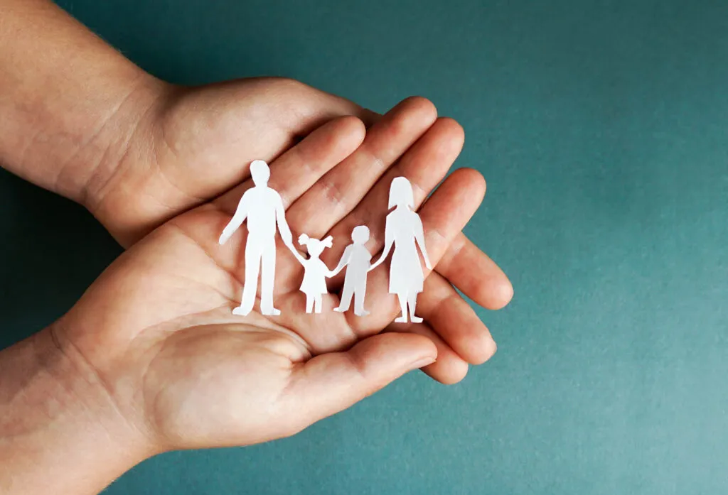Kupade händer som håller en familj, utklippt i papper, i handflatan. Symbolisk bild för Sociala Missionens stöd till familjer som vill återförenas i Sverige.
