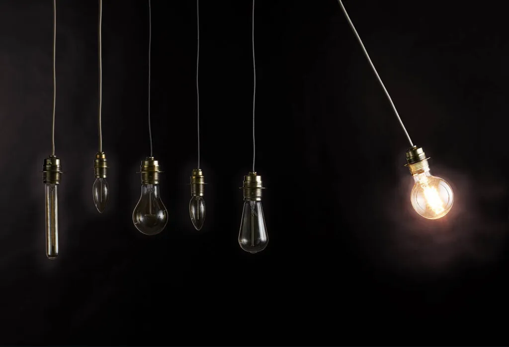 En lysande glödlampa hängande och i fart mot fem andra släckta glödlampor, som symbolisk bild för kunskap och fortbildning av kunskapen i utbildningen Livsnära Samtal.