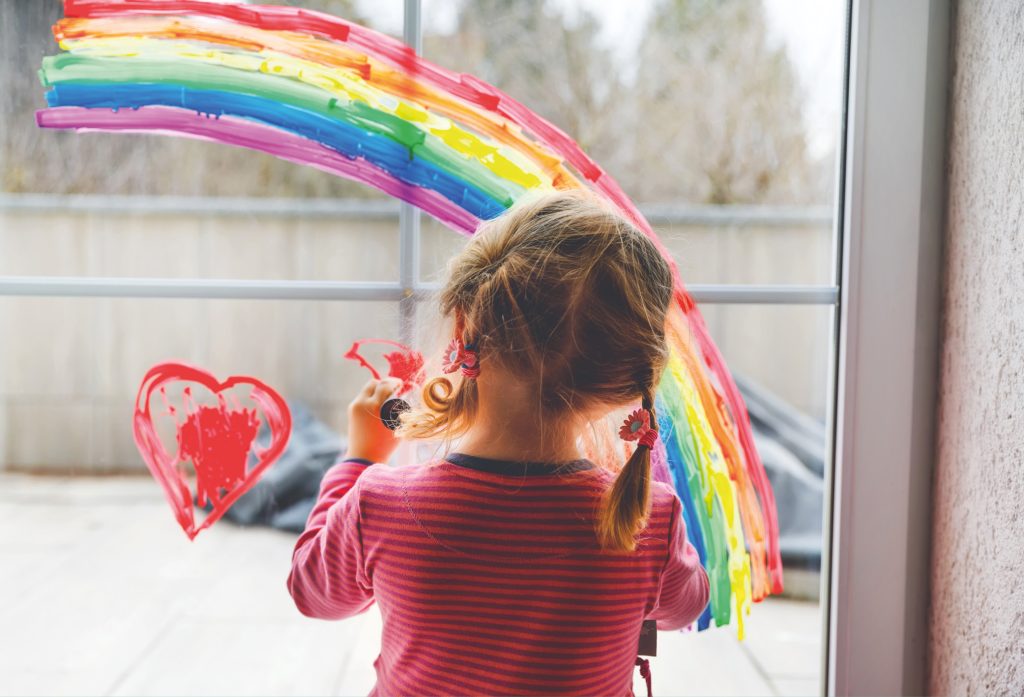 Bild på ett barn, liten flicka, bakifrån som målar med färg på ett fönster. Hon har målat en regnbåge och två hjärtan. Symbolisk bild för projekt Familjestöd – ett ny satsning för att kunna nå fler barnfamiljer i utsatthet med gratis juridisk hjälp för att kunna bryta utsattheten.