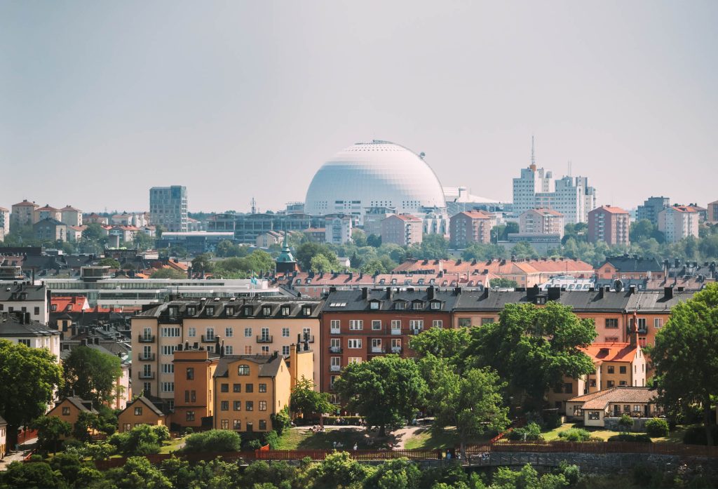 Bild över Stockholms stad som siluett med grönskande träd i förgrunden med bostäder och globen i bakgrunden