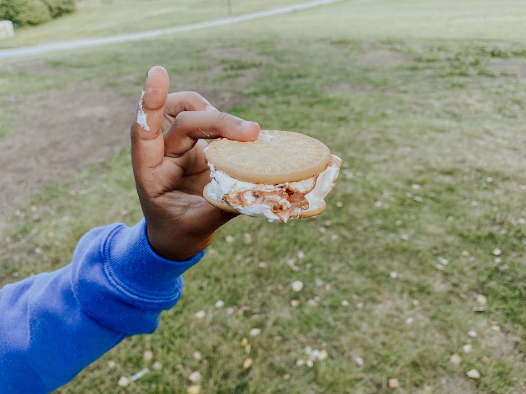 Närbild på ett barns hand som håller upp ett mariekex med smält marshmallows från Sociala Missionens förra sommarläger för barn och föräldrar sommaren 2024.